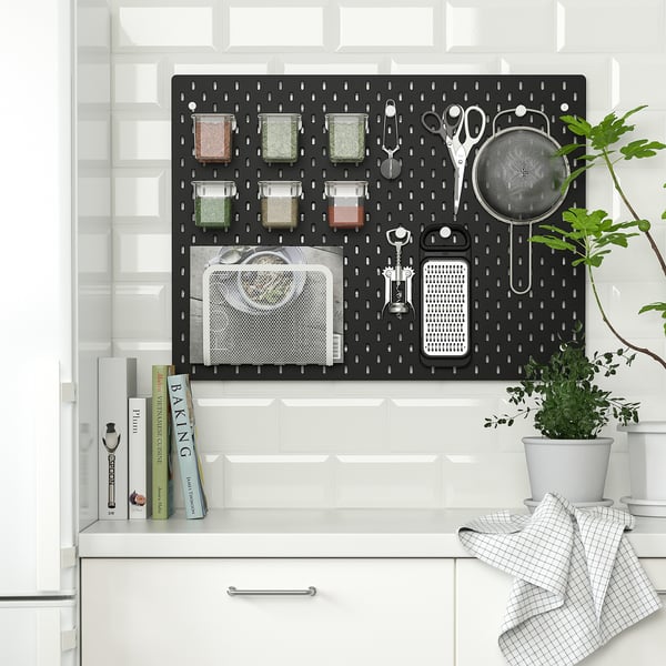 Kitchen pegboard organiser with spices, utensils, and tools, mounted on a tiled wall.
