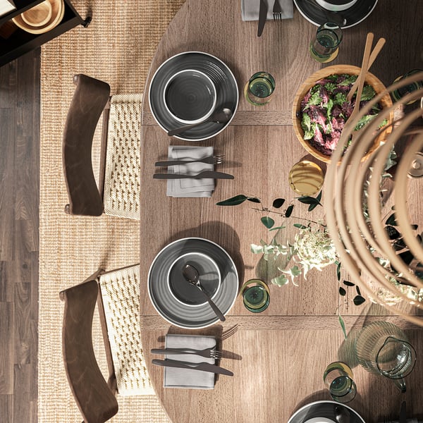 Wooden round dining table set for four with plates, glasses, cutlery, and salad.