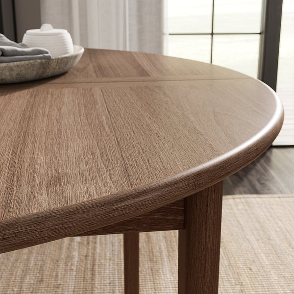 Wooden round dining table with light brown finish, smooth edges, and visible graining patterns.