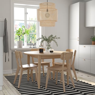 SKANSNÄS dining set with extendable round table, four armless chairs, pendant light, and black/white rug in bright kitchen.