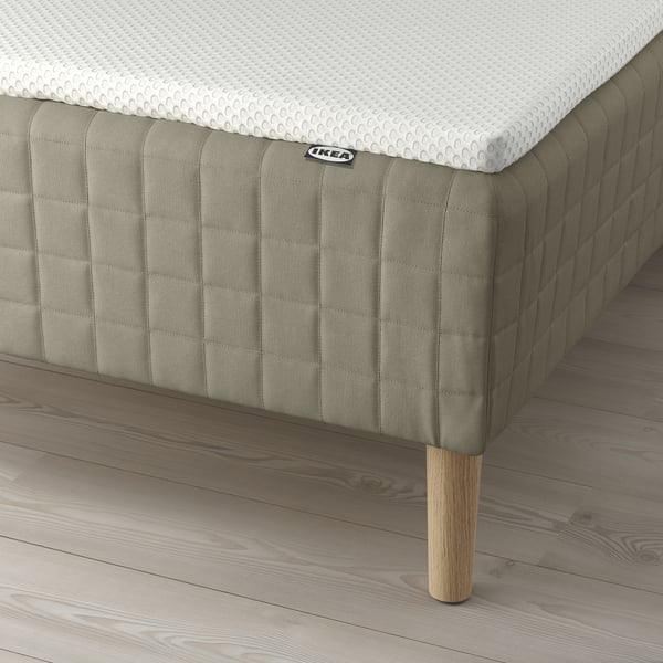 A bed with a SKÅRER sprung mattress, wooden legs, and a white mattress pad.