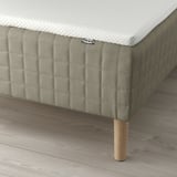 A bed with a SKÅRER sprung mattress, wooden legs, and a white mattress pad.