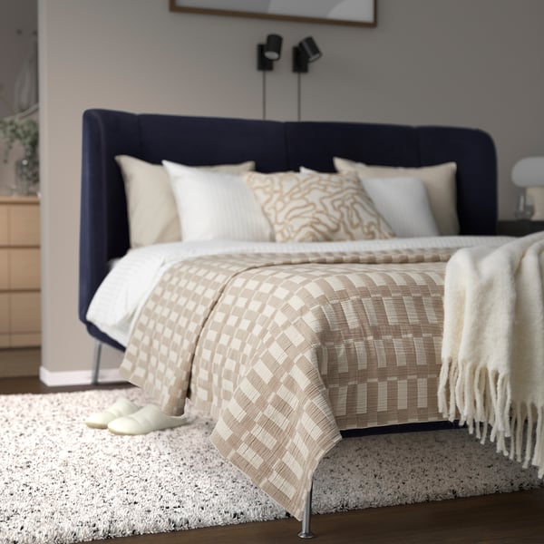 Modern bedroom with navy upholstered headboard, neutral bedding, and a cozy rug. Small nightstands and minimalist decor.