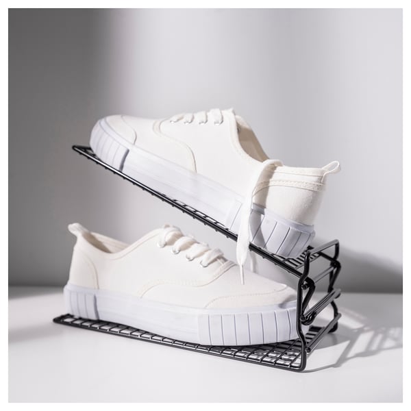 A pair of white sneakers sit on a black metal shoe rack, saving space with adjustable shelves.