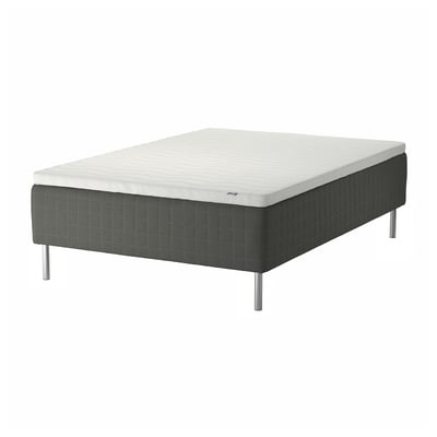 Depicts a SKOTTERUD bed set with a white mattress and a dark grey upholstered base on stainless steel legs.