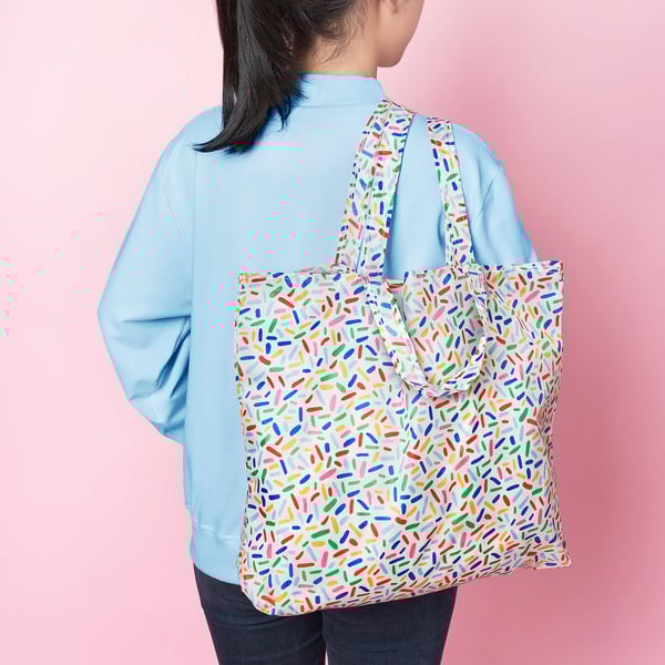 Multi-use bag with sprinkle pattern, folds into pocket, ideal for shopping/travel.