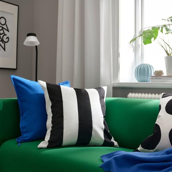 Bright green sofa featuring a black and white striped cushion cover, SLÅNHÖSTMAL, along with blue accents. A modern, minimalist design.