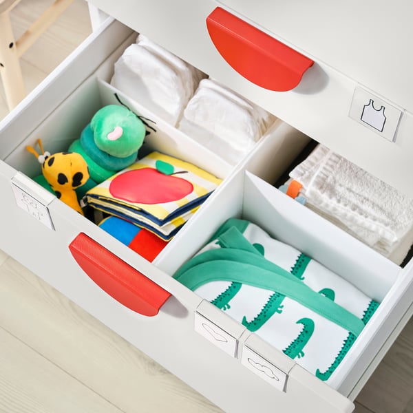 White SMÅSTAD storage with red handles, organized with childrens items like diapers, books, and clothes.