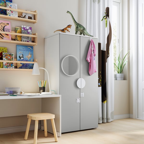 Kids room with grey SMÅSTAD wardrobe, wooden shelves, dinosaur toys, and white desk.