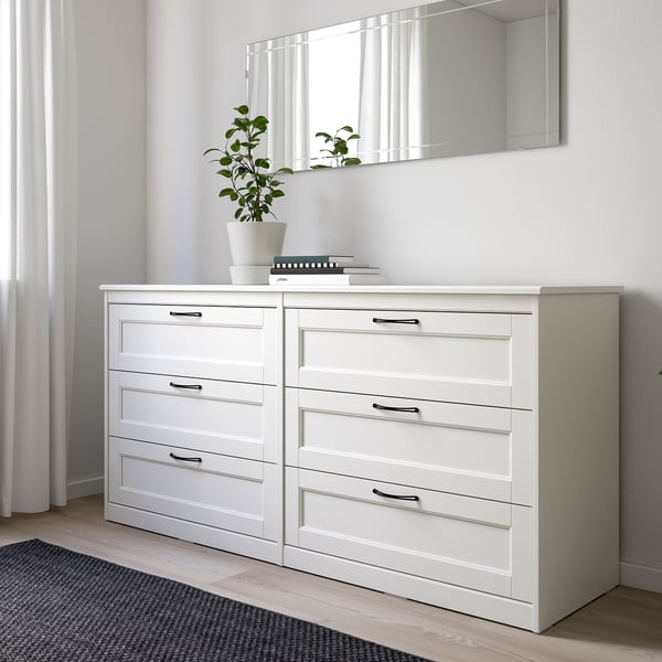 White SONGESAND dresser in minimalist bedroom with six drawers and plant, beside window.