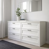 White SONGESAND dresser in minimalist bedroom with six drawers and plant, beside window.