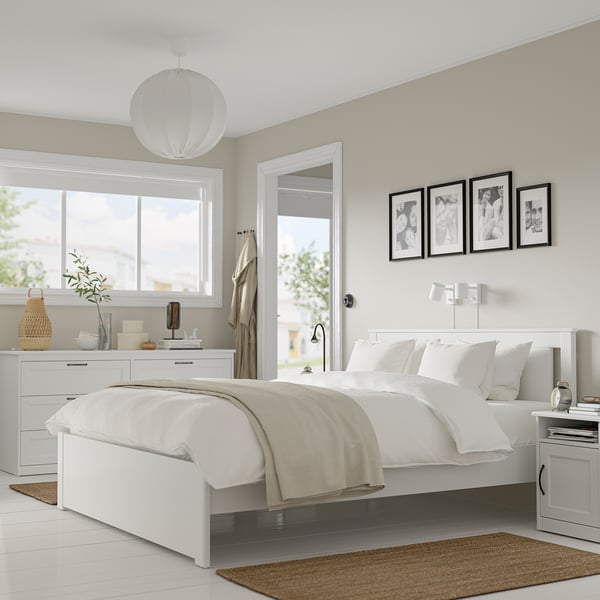Modern white bedroom SONGESAND bed, drawers & tables. Clean, classic design with high legs. Large bed dominates space, flanked by smaller furnishings.
