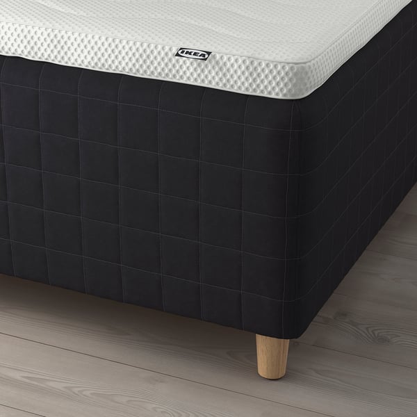 A modern bed setup with a black frame. It includes a white mattress with pocket springs for support and comfort. The frame has wooden legs.