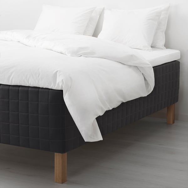 Modern bed with black quilted wooden-base mattress, white sheets, and wooden legs.
