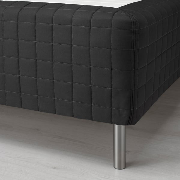 Black quilted sofa corner on wooden floor, showing metal leg.