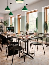 Modern café with square STENSELE tables in black, green pendant lights, large windows, and cacti.