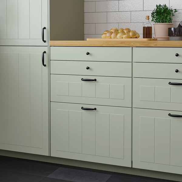 Modern kitchen with green cabinets, black handles, bread, bottles, plant.