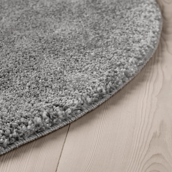 Close-up of a soft, plush round rug in light gray on a wooden floor, showcasing its dense, textured pile.