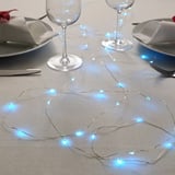 Table setting with blue led string lights, plates, glasses, and cutlery.