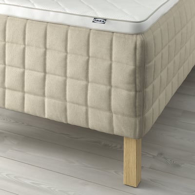 Close-up of a stylish bed with textured linen sides. Linen creates subtle variations if seen up close. The beds wooden leg is visible.