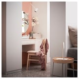 A narrow white dressing table with a glass top and wood chair beside a bed in a bedroom.