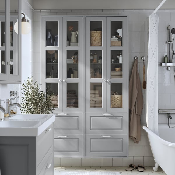 Grey TÄNNFORSEN cabinet with glass doors and drawers in bathroom next to bathtub and sink.