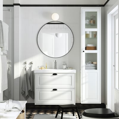 Modern white bathroom with TÄNNFORSEN vanity, round mirror, tall cabinet, and black/white floor tile.