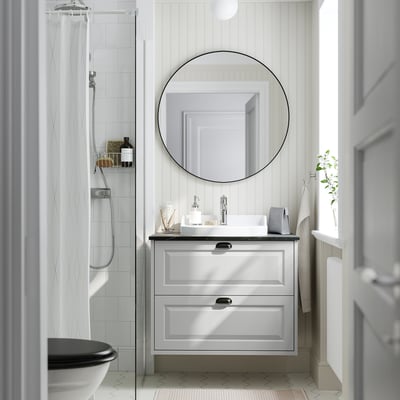 Modern gray bathroom vanity, round mirror, white sink & toilet. Tiles & shower.