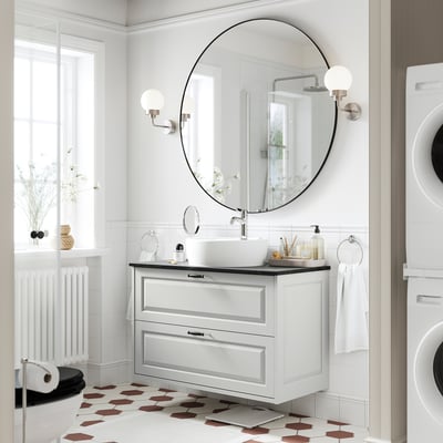 A modern bathroom with a TÄNNFORSEN light grey vanity. It has a round basin and drawers, with spherical sconces and hexagonal floor tiles.