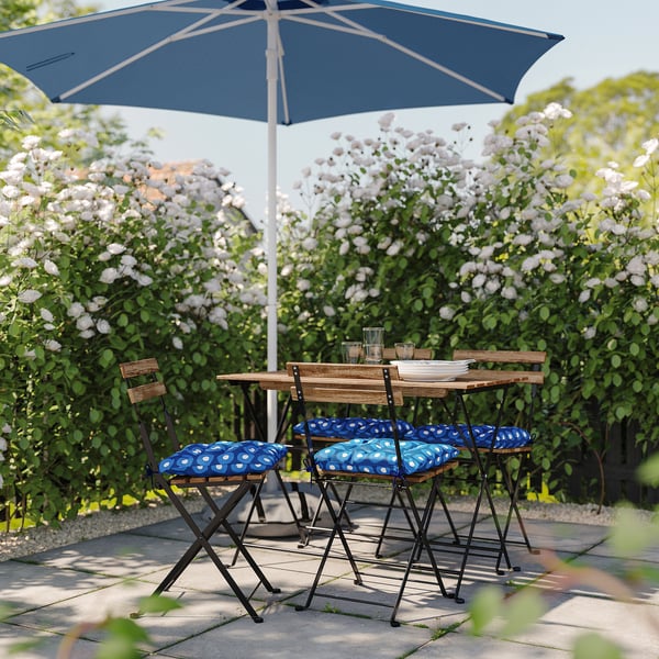 Patio setup with blue & white polka dot cushioned chairs, wooden table, and navy umbrella under blooming white flowers.