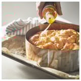 Person drizzling honey on golden brown baked treat in round metal pan.