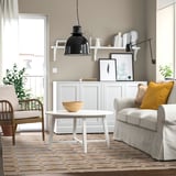 An earthy geometric rug in beige and grey under a white coffee table, with a grey couch and black pendant lamp nearby.