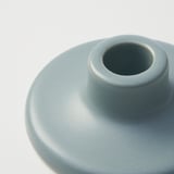 Close-up of smooth, glazed blue stoneware candlestick with round base.