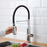 Person turning on TOLLSJÖN faucet, water sprays from handspray, apples in sink.