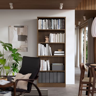 Modern living room with TONSTAD bookcase, oak veneer, black armchair, wooden chairs, and plant.