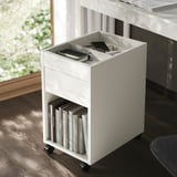 Small white mobile storage unit with drawer, holding books below and tech items on top, ideal for organizing office space.