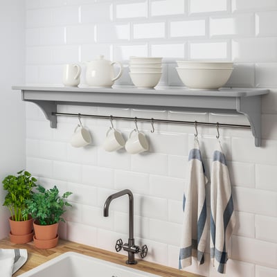 Kitchen shelf with hanging mugs and towels, holding dishes and teapot.