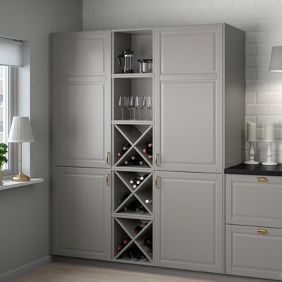 A large grey TORNVIKEN kitchen cabinet with wine storage, featuring glass doors, holding bottles and wine glasses, next to a counter with decor.