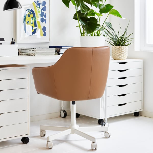 Tan leather office chair with curved back & white star-base next to desk, books, plants