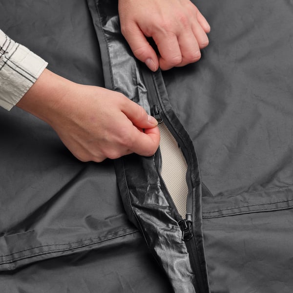 Person zipping black TOSTERÖ waterproof cover, protecting outdoor furniture.