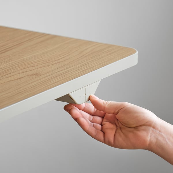 A hand adjusting the tilt lock on the edge of a wooden top desk, showcasing its height-adjustable feature.
