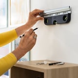 Person adjusts magnetic spirit level on wall, using pencil to mark spots for precise alignment, demonstrating its utility in diy projects.