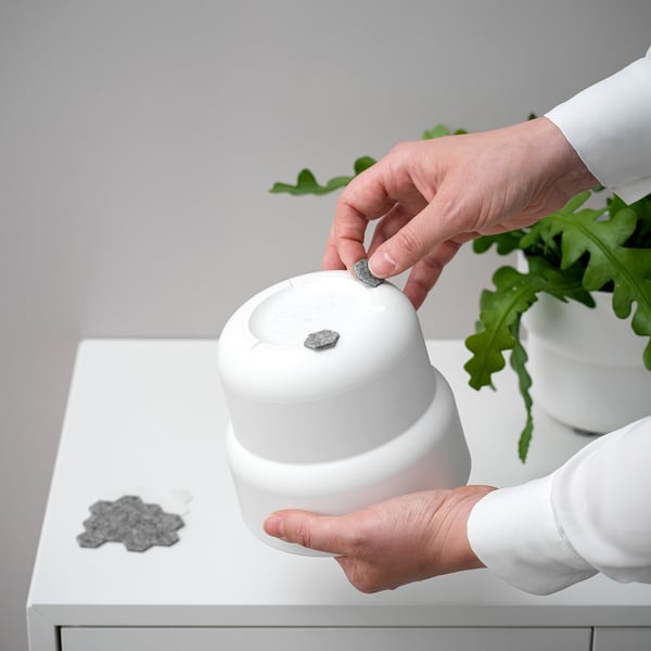 Person placing small, round, self-adhesive felt pads onto white furniture to prevent scratches and ease furniture movement.