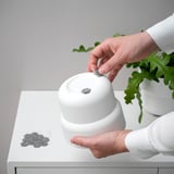 Person placing small, round, self-adhesive felt pads onto white furniture to prevent scratches and ease furniture movement.