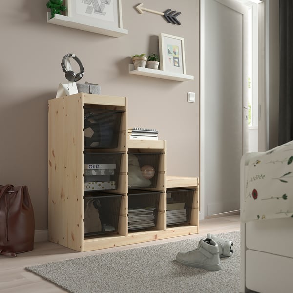 Light-colored wooden TROFAST storage unit with mesh boxes, holding various items, placed near a doorway and white furniture.