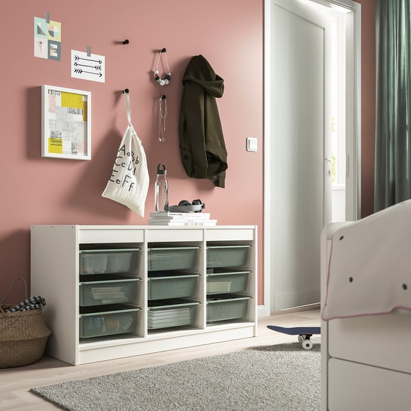 TROFAST storage unit in white with mesh boxes, skateboard & hooks against pink wall.