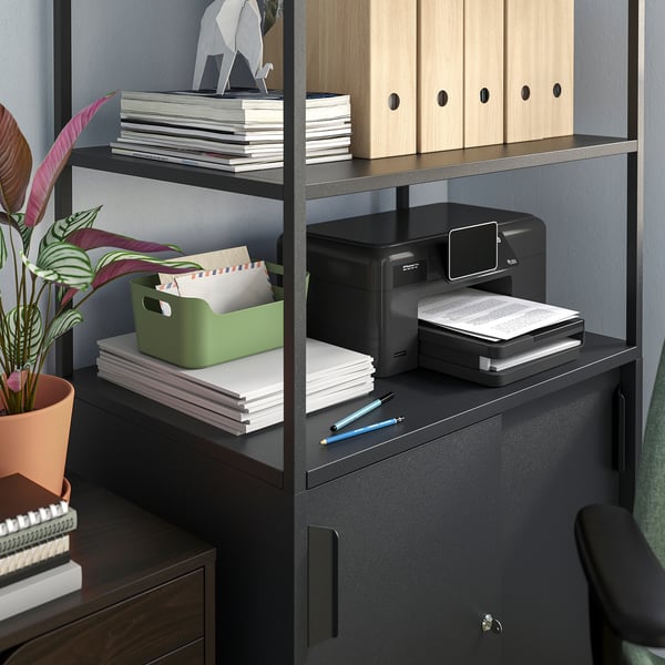 Office setup with trottén storage shelves, green box, printer, stack of papers, pens, and plant.