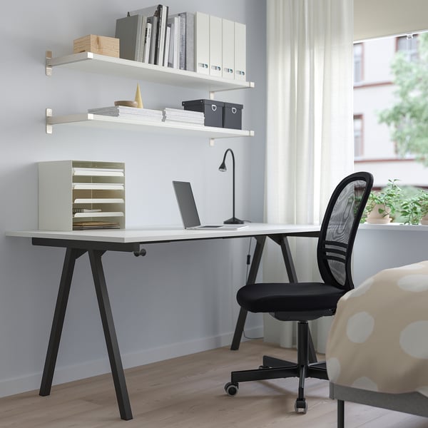 White TROTTEN desk with black legs, minimalist design, laptop, office supplies, black mesh chair, large window.