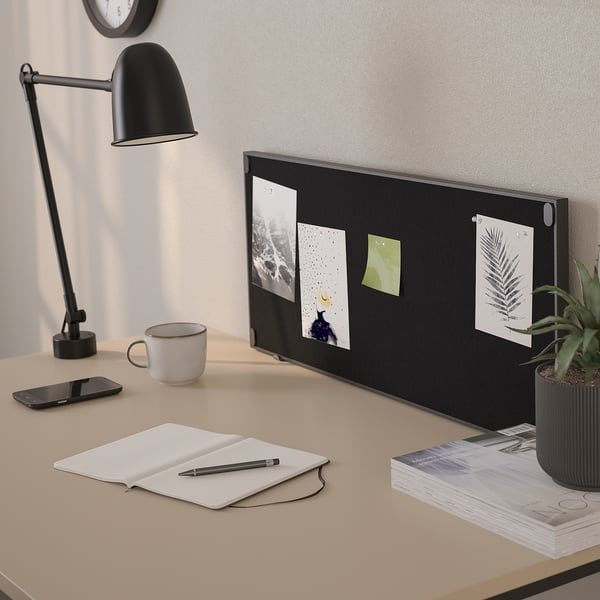 Desk setup with notice board, lamp, cup, phone, notebook, pen, and plants.
