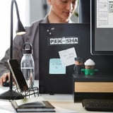 A workspace with a TROTTEN double-sided notice and whiteboard, mounted on a desk. It holds papers, notes, and small decorations, aiding organization.